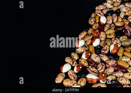 Verschiedene Bohnen auf dem Tisch verstreut. Natürliche Produkte auf dunklem Hintergrund. Stockfoto