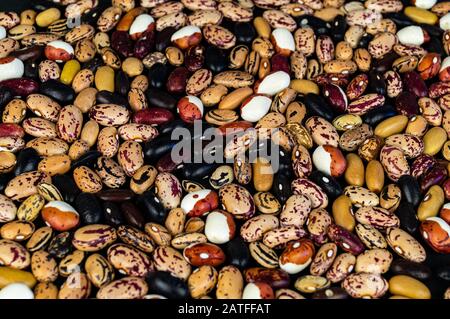 Verschiedene Bohnen auf dem Tisch verstreut. Natürliche Produkte auf dunklem Hintergrund. Stockfoto