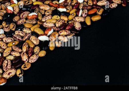 Verschiedene Bohnen auf dem Tisch verstreut. Natürliche Produkte auf dunklem Hintergrund. Stockfoto