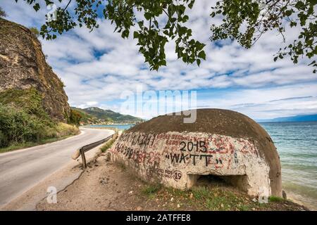 Unter dem kommunistischen Diktator Hoxha errichteter, mit Graffiti bedeckter Bunker am Ohridsee, mazedonisches Ufer in der Ferne, in der Nähe von Pogradec, Albanien Stockfoto