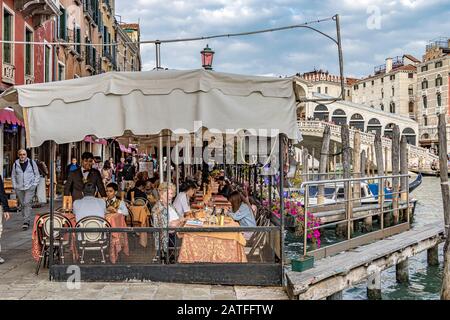 Die Leute essen in einem Restaurant in der Nähe der Rialto-Brücke, der ältesten der vier Brücken, die den Canal Grande in Venedig, Italien überspannen Stockfoto