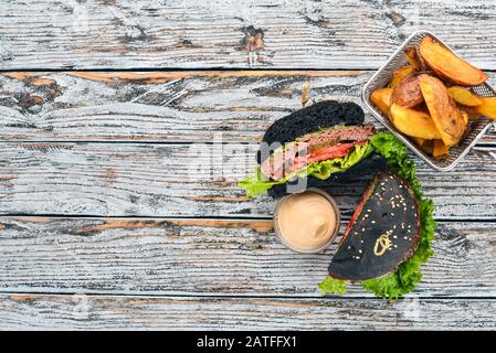 Gebackene Kartoffeln und Burger mit Fleisch, Tomaten und Zwiebeln. Auf Holzgrund. Freier Speicherplatz für Text. Draufsicht. Stockfoto