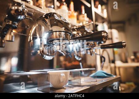 Flache Schärfentiefe (selektiver Fokus) mit einer professionellen metallischen Tasse Kaffee- und Espressomaschine in einem Coffeeshop. Stockfoto