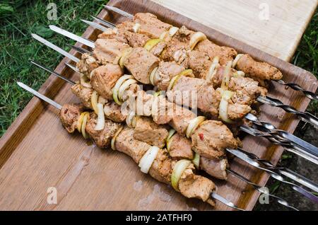 Marinierte rohe Schweinefleischspieße mit Zwiebelringen auf Spießen. Grill Mit Köstlichem Gegrilltem Fleisch. Nahaufnahme. Kochfleisch für Grillparty. Stockfoto