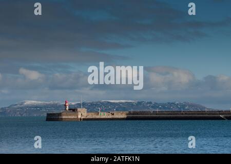 Das Leuchthaus in Dun laoghaire Hafen mit Hügel von Howth Abdeckung durch Schnee, Irland Stockfoto