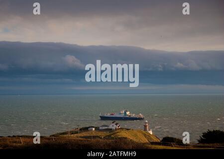 Der Baily Leuchtturm, Howth. co. Dublin, Baily Leuchtturm auf Howth Klippen, Blick auf den Baily Leuchtturm von der Klippe mit Frachtschiff im Hintergrund Stockfoto