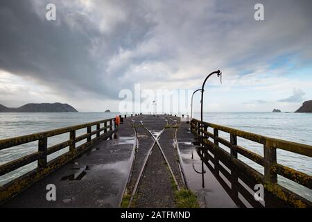 Blick von der längsten Wharf (Tolaga Bay) in Neuseeland mit dramatischen Wolken und Reflexionen in einer Pfütze entlang von Bahngleisen und Kränen. Stockfoto