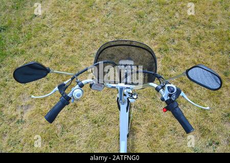 Elektrofahrrad Ruder oder Helm im Park auf sonnigen Sommertag. Von oben geschossen. Die Ansicht von e bike Lenkrad mit Glocke, Bremsen, Geschwindigkeit schalten, eine Stockfoto