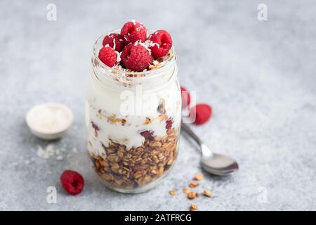 Joghurt mit Granola und Himbeeren im Mixbecher auf Betongrund. Gesundes Frühstück oder Snack für unterwegs Stockfoto