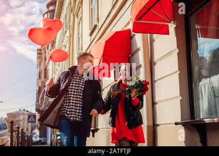 Valentinstag Paar. Mann und Frau laufen mit Blumenstrauß aus Rosen Blumen und Ballons auf der Straße der Stadt. Stockfoto