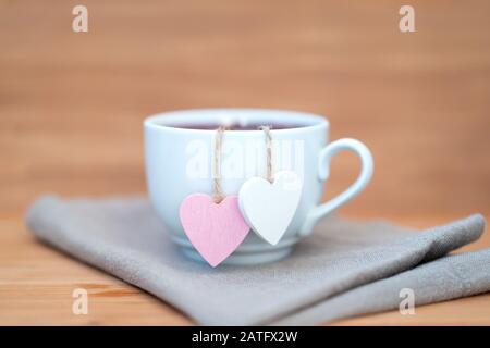 Herzförmige Teetasche in weißer Tasse Tee - süße Liebeserklärung auf Holzhintergrund, selektiver Fokus. Valentines Tageskonzept. Tasse Tee für zwei Liebhaber Flitterwochen Hochzeit Morgen Überraschung Frühstück Stockfoto