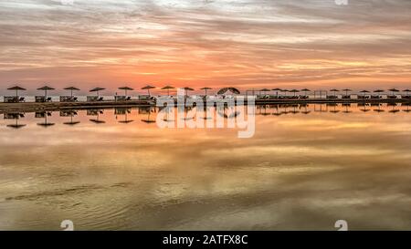 Sonnenliegen und Sonnenschirme stehen an einer Bank im roten Meer in einer langen Reihe bei Sonnenuntergang, El Gouna, Ägypten, Jnuary 16, 2020 Stockfoto