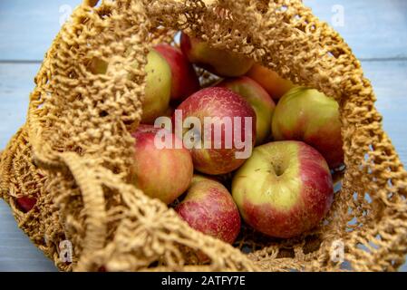 Frische Äpfel in einem gewebten Sack wiederverwendbares, umweltfreundliches Produkt. Auf blauem Holzhintergrund. Stockfoto