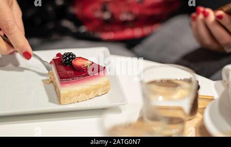 Frau, die in einem Café Käsekuchen isst und Kaffee trinkt. Käsekuchen mit Erdbeere und brombeere. Kaffeepause. Stockfoto