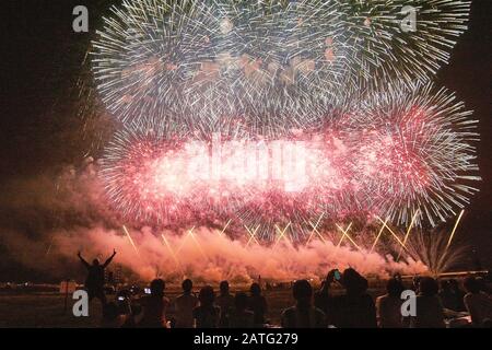 Zuschauer sehen beim Nagaoka Fireworks Festival 2017 ein schönes Feuerwerk in Rot und Weiß. Ein älterer Mann setzt zwei Friedenszeichen. Stockfoto