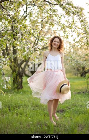 Junge attraktive Frau mit lockigem Haar wandern in einer grünen blühenden Garten. Feder romantische Stimmung. Stockfoto