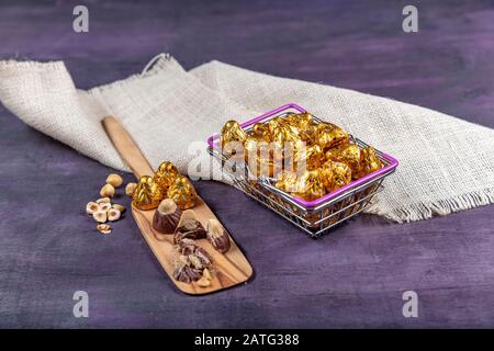 Eine Schachtel Pralinen in goldener Folie. Große Schachtel Schokoladenkäuze in Goldfolie steht auf einem violetten Holzhintergrund. EID al-Fitr (fest des Ramadan) konce Stockfoto