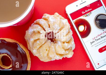 Eine Tasse Kaffee mit Chocolate Dip Donut und Honey Cruller Donut mit einem iPhone Plus und der Tim Hortons App Stockfoto