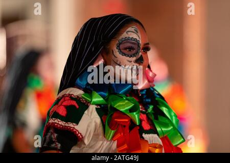 Indianapolis, Indiana, USA - 2. November 2019: Day of the Dead, junge mexikanische Frauen mit Gesichtsfarbe am Schädel, die traditionelle Kleidung tragen und TR durchführen Stockfoto