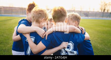 Glückliche Kinder im Grundschulsportteam feiern im Turnier-Endspiel den Fußballerfolg. Kinder Fußballmannschaft versammelt sich in einem Kreis Stockfoto