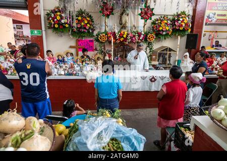 Oaxaca de Juarez, Mexiko. Februar 2020. Fr. Hector Zavala Balboa feiert die Messe auf dem Sanchez Pascuas Nachbarschaftsmarkt an der Dia de la Candelaria und feiert 40 Tage nach der Geburt Jesu. Familien verkleiden Puppen des Baby-Jesus und bringen sie zur Masse, um gesegnet zu werden. Kredit: Jim West/Alamy Live News Stockfoto