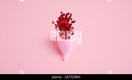 Wiederverwendbarer Menstruationsbecher mit rotem Konfetti auf pinkfarbenem Hintergrund. Alternative Menstruationshygiene. Kritische Tage, Menstruationszyklus, weibliches h Stockfoto