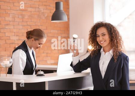 Junge Frau mit Schlüssel vom Zimmer an der Rezeption im Hotel Stockfoto