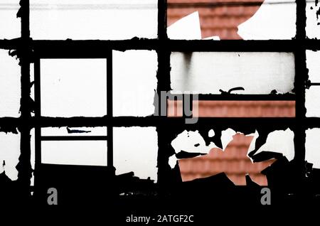 Altes Fenster mit zerbrochenem Glas, durch die Löcher: Ein Dach mit Kacheln Stockfoto