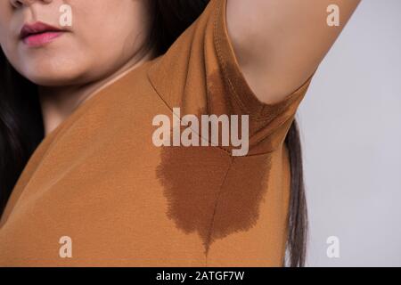 Close-up asiatische Frau mit Hyperhidrose schwitzen. Junge Asien Frau mit Schweiß Flecken auf Ihrer Kleidung vor grauem Hintergrund. Healthcare Konzept. Stockfoto