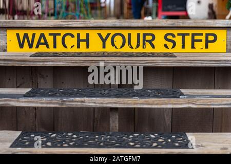 Gelbes Warnschild, beobachten Sie Ihren Schritt auf einer Holztreppe Stockfoto