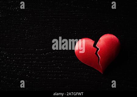 Gebrochenes rotes Herz auf schwarzem Holzhintergrund. Herz gebrochen, Liebe und Valentines Tageskonzept. Stockfoto