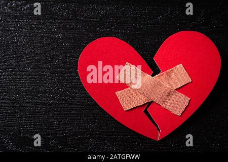 First Aid Band Gepolsterter Gipsstreifen Medical Patch auf rotem Herzpapier auf Holzhintergrund geklebt. Herz gebrochen, Liebe und Valentines Tageskonzept. Stockfoto