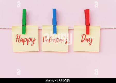 Fröhlicher Text zum Valentinstag auf hängenden Papiernotiz. Rosafarbener Hintergrund. Stockfoto