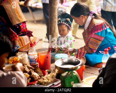 Eine Frau und ein Kind der Blume H'mong (Flower Hmong) im traditionellen Kleid teilen sich einen Moment über eine Mahlzeit auf dem Bac ha Markt in Bac ha, Lao Cai, Vietnam. Stockfoto