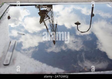 Urbane Reflexion: Ein Lichtpfahl, ein Kran und ein Himmel mit Wolken, die sich auf der Wasseroberfläche in einer Pfütze in Puerto Madero, Buenos Aires, Ar widerspiegeln Stockfoto