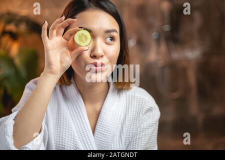 Lustige asiatische Mädchen posieren für Kamera mit Gurkenscheiben Stockfoto