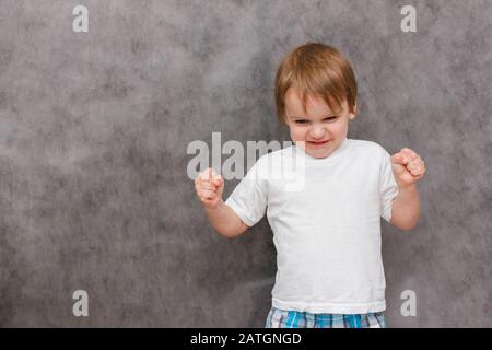 Wütend Junge zeigt seine Armmuskeln. Porträt des Jungen des europäischen Auftritts auf grauem Hintergrund. Konzept der Elternschaft Probleme Stockfoto