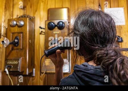 Ein junger Mann, der über ein 1900er Holzwandtelefon telefonieren kann. Der Mensch ruft die Vergangenheit an. Vintage-Telefon im Museum, Kootenays, British Columbia, Kanada Stockfoto