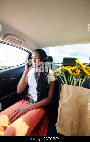 Positive junge Frau sitzt auf dem Rücksitz im Taxi und telefoniert, wenn sie nach dem Lebensmittelgeschäft nach Hause kommt Stockfoto