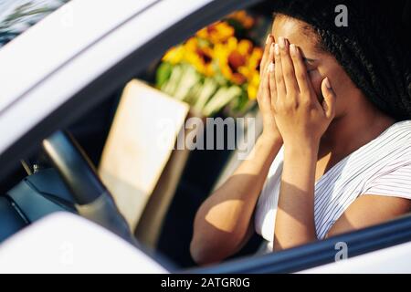Junge Frau, die Gesicht mit Händen bedeckt, während sie Angst hat, nachdem sie in einem anderen Auto gestürzt ist Stockfoto