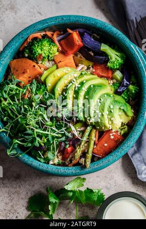 Vegane Mittagsschüssel. Gebackenes Gemüse, Quinoa und Avocadosalat in blauem Gericht, dunkler Hintergrund. Stockfoto