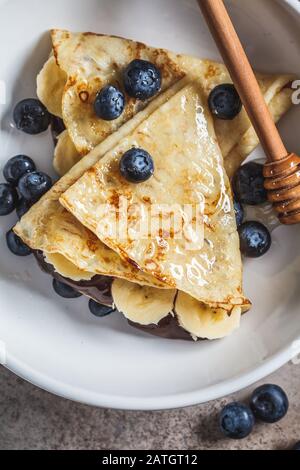 Pfannkuchen mit Schokolade, Früchten und Honig in einem weißen Teller. Stockfoto