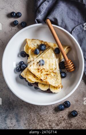 Pfannkuchen mit Schokolade, Früchten und Honig in einem weißen Teller. Stockfoto