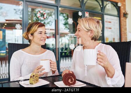 Frau und ihre Erwachsene Tochter haben Kaffee und Desserts im Café und diskutieren über Neuigkeiten Stockfoto