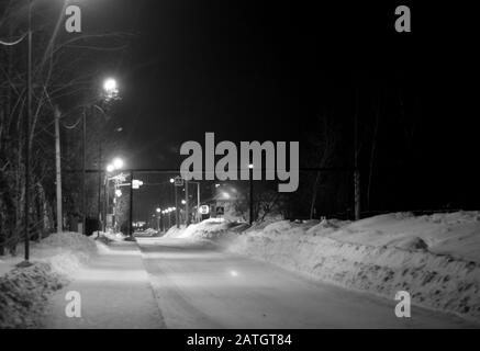 Dunkle Gasse, die von mehreren Laternen an einem ruhigen Winterabend beleuchtet wird, Schwarz-Weiß-Bild. Stadtlandschaft. Stockfoto