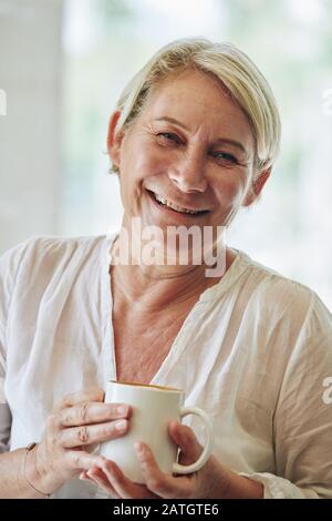Porträt einer lächelnden reifen Frau, die einen großen Becher Morgenkaffee hält Stockfoto