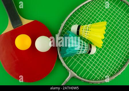 Tischtennisschläger und Badminton, bunte Bälle und Absperrhähne auf grünem Hintergrund Stockfoto