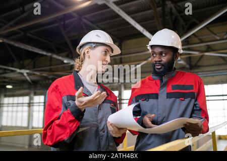 Nachdenkliche junge multiethnische Arbeiter in Hardhats diskutieren über den Bebauungsplan auf der Baustelle Stockfoto