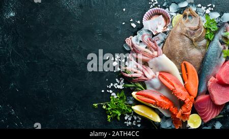 Frische Meeresfrüchte und Fisch auf schwarzem Steingrund. Flunder, Hummer, Tintenfisch, Thunfisch, Fisch. Draufsicht. Freier Speicherplatz. Stockfoto