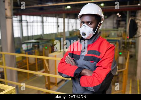Porträt eines selbstbewussten jungen Afrikaners in Atemschutzmaske und Hardhat, der in der Giftindustrie arbeitet Stockfoto